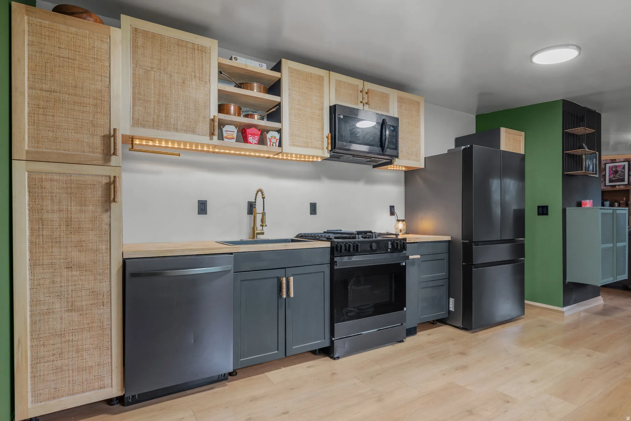 Contemporary kitchen featuring light wood-finish flooring, dark gray cabinetry, and black appliances