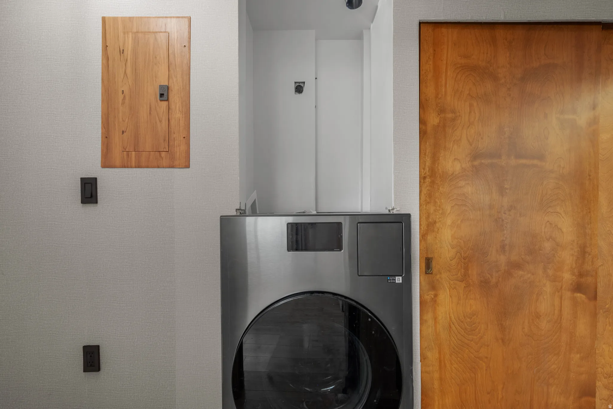 Dedicated laundry area featuring a stainless steel front-load washing machine, a wooden utility door, and a matching wooden electrical panel cover