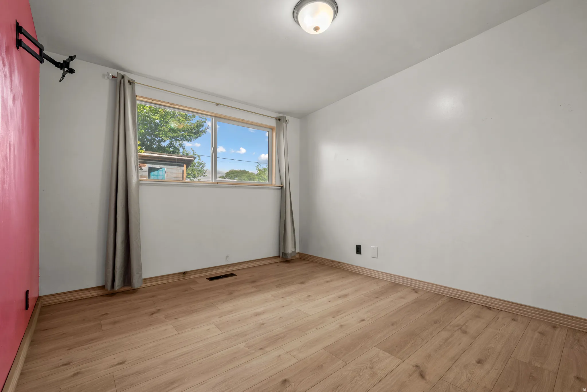 Room featuring wood-finish flooring, a window with natural light, a ceiling-mounted light fixture, and a contrasting accent wall