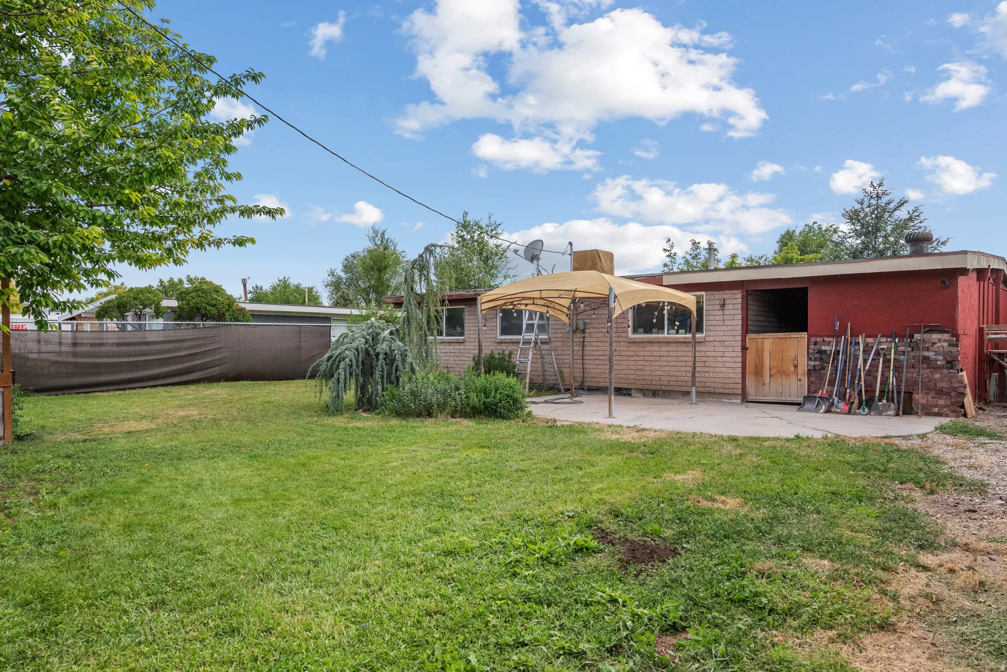 Expansive backyard featuring a concrete patio, a red building with a large opening, and a brick-faced structure with windows