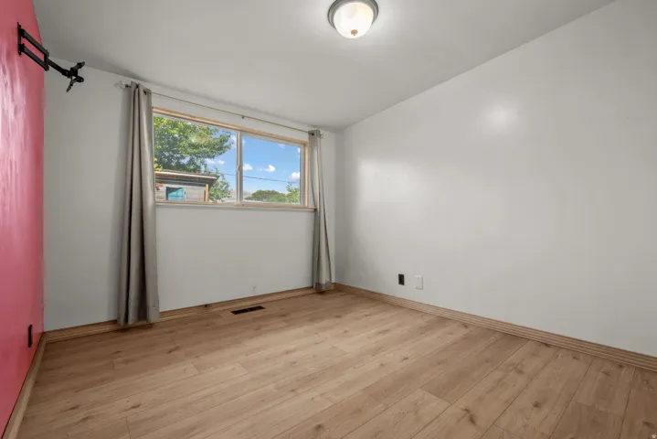 Room featuring wood-finish flooring, a window with natural light, a ceiling-mounted light fixture, and a contrasting accent wall