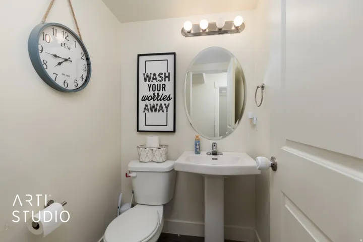 Pedestal sink with a wall-mounted oval mirror and a four-bulb vanity light fixture