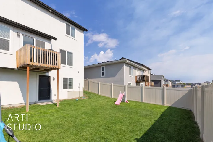 Expansive backyard featuring a manicured lawn, full fencing, a ground-level exterior door, and an upper-level wood deck