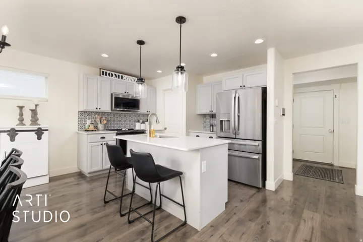 Kitchen featuring a central island with countertop seating, light-toned cabinetry, stainless steel appliances, patterned tile backsplash, and wood-finish flooring