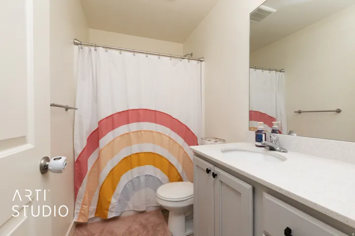 Bathroom featuring a built-in vanity with a white countertop and undermount sink, a large wall-mounted mirror, and a toilet with an adjacent shower area