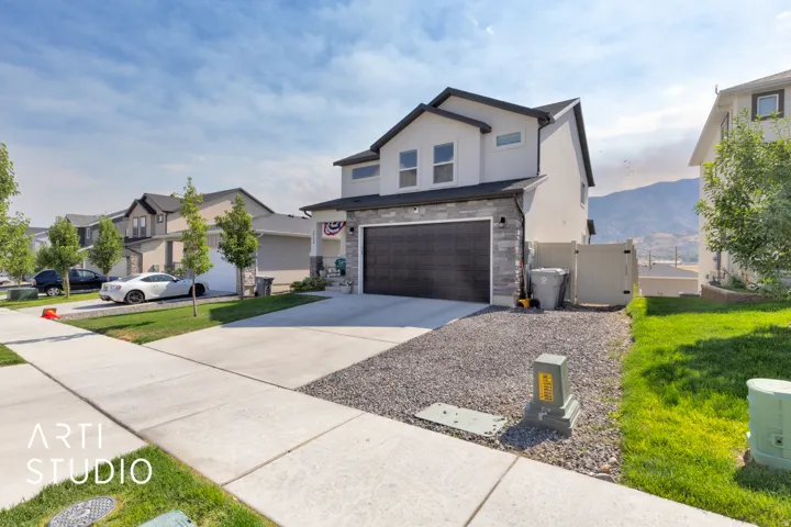 Contemporary two-story residence featuring a dark garage door, stone facade accents, and a light-toned exterior