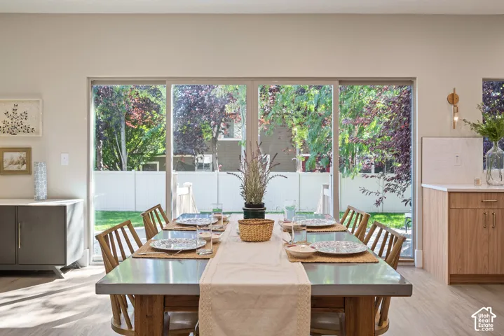 Window-lined dining area offers abundant natural light and flexible seating options. The absence of a center chandelier allows the space to adapt easily to different table arrangements.