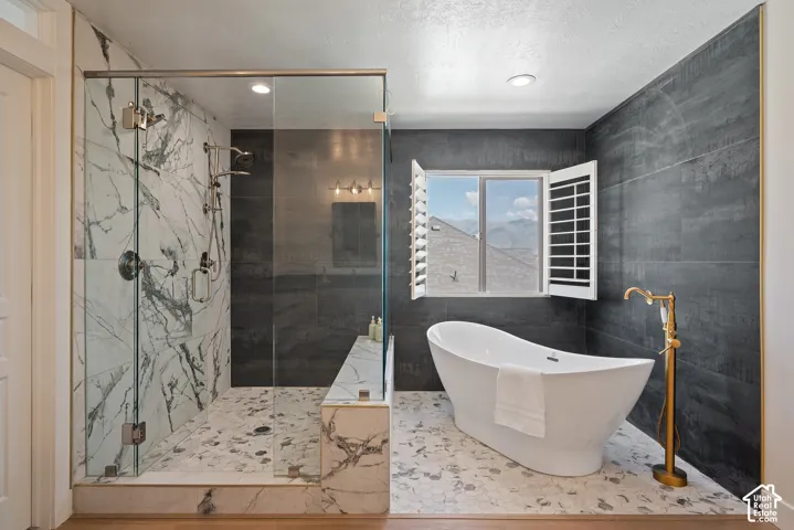 Beautifully tiled wet-room shower featuring three full-body spray heads, built-in bench seating, and custom glass panels extending to the ceiling for a warm, immersive experience.