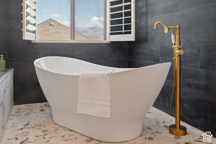 Deep, angled freestanding soaking tub paired with complementary brass fixtures and positioned beneath a plantation-shuttered window for natural daylight or a cozy evening atmosphere.