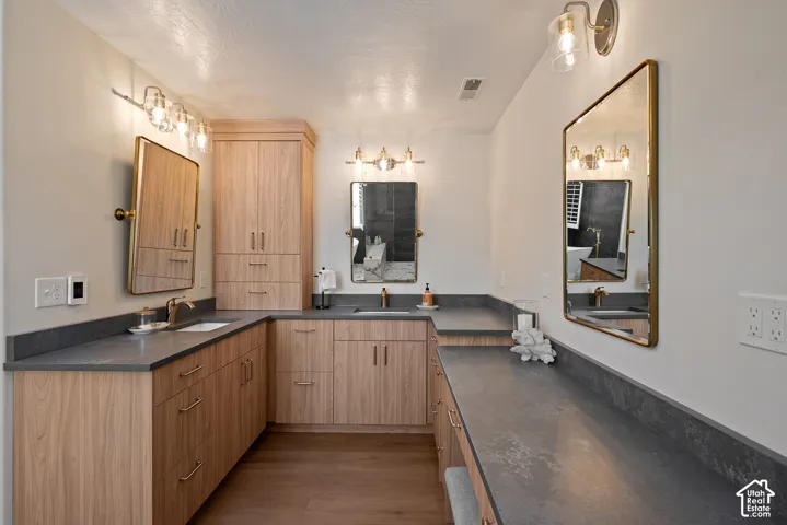 Primary bath featuring warm wood tones, generous cabinetry, quartz countertops, and heated plank flooring for an added touch of comfort.