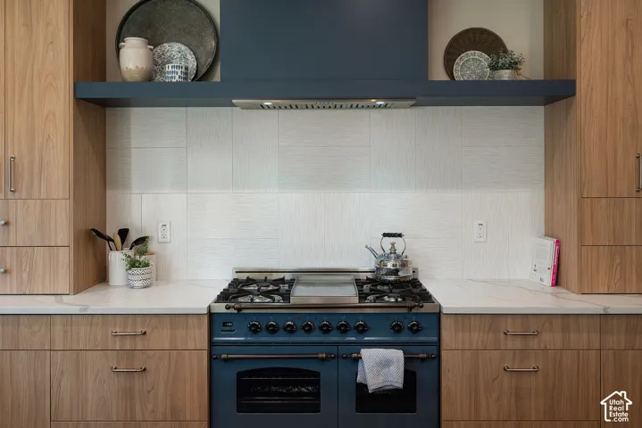Chef-inspired kitchen with a tasteful patterned tile backsplash, concealed outdoor-vented hood, and a distinctive colored flue that adds designer character. No microwave over the range keeps the cooking area clean and streamlined.