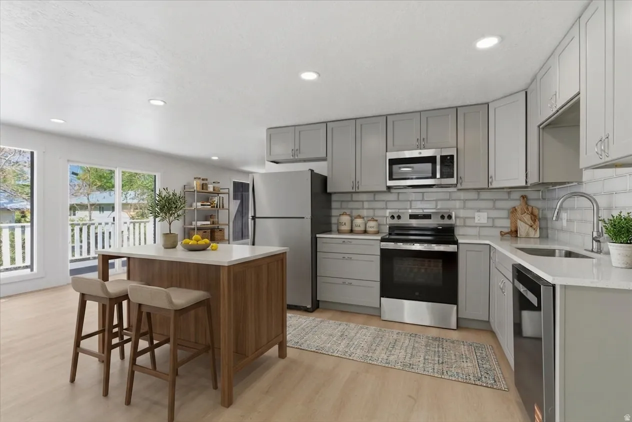 Modern kitchen featuring light gray shaker cabinetry, stainless steel appliances, a white subway tile backsplash, and light wood-finish flooring