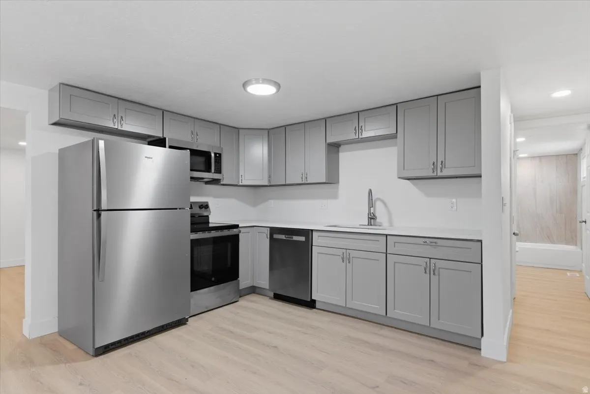 Kitchen featuring light gray cabinetry, white countertops, stainless steel appliances, and light wood-finish flooring