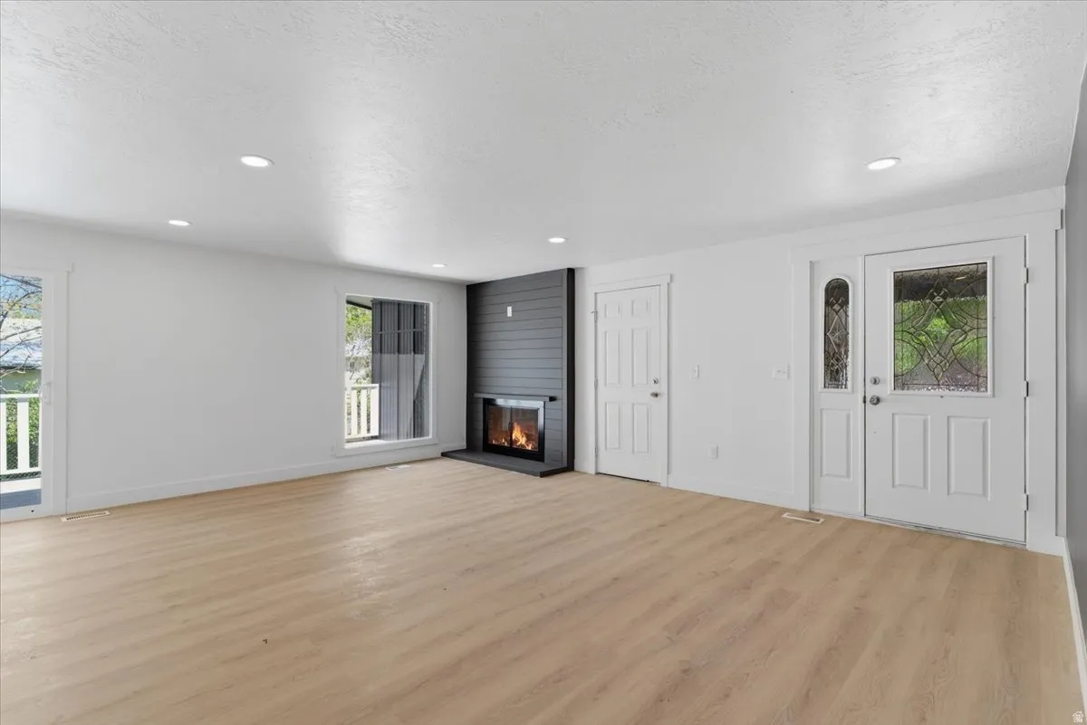 Spacious room featuring light wood-finish flooring, a modern fireplace with a dark shiplap surround, and recessed ceiling lighting
