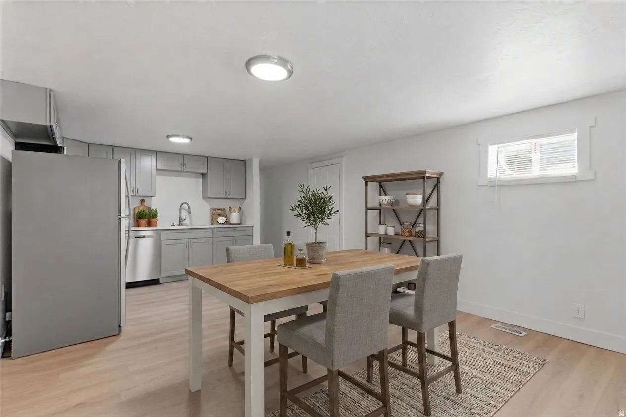 Open-concept kitchen and dining area featuring light wood-finish flooring, recessed ceiling lighting, gray cabinetry, stainless steel appliances, and a compact window with white trim