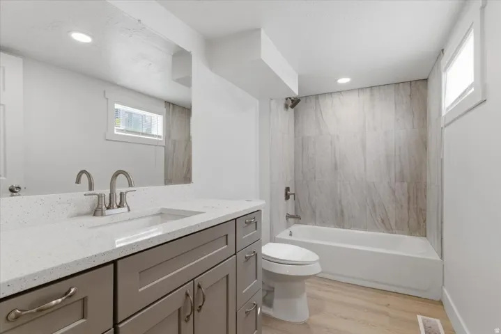 Bathroom featuring a single vanity with grey cabinetry, a light-colored solid surface countertop, and a rectangular undermount sink with brushed nickel fixtures