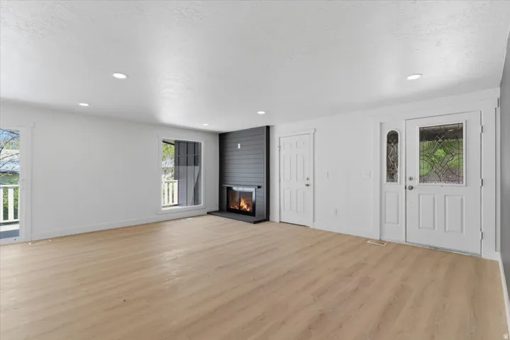 Spacious room featuring light wood-finish flooring, a modern fireplace with a dark shiplap surround, and recessed ceiling lighting