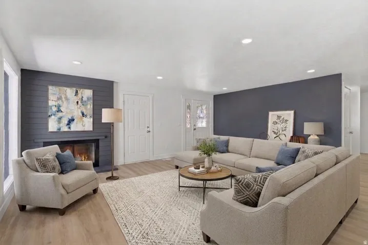 Living room featuring wood-finish flooring, a fireplace with dark shiplap surround, white trim throughout, and recessed lighting
