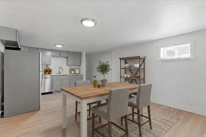 Open-concept kitchen and dining area featuring light wood-finish flooring, recessed ceiling lighting, gray cabinetry, stainless steel appliances, and a compact window with white trim