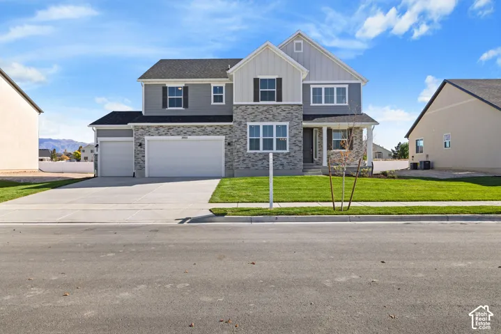 Two-story exterior featuring a stone facade, horizontal and vertical siding, a three-car garage, and a manicured front lawn
