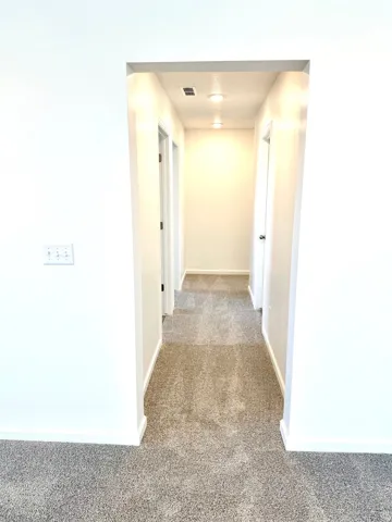 Carpeted hallway with flush-mount lighting and white walls