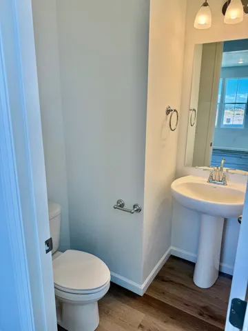1/2 bath across from the office towards the front of the home with a pedestal sink with chrome faucet, wall-mounted mirror, overhead vanity lighting, and LVT flooring