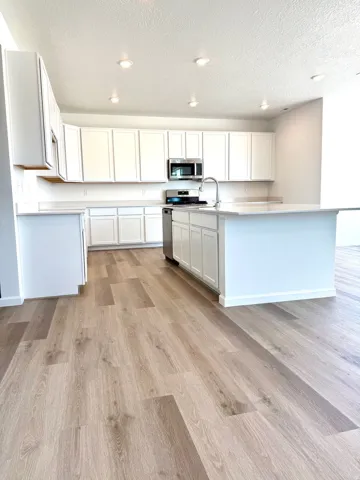 Kitchen featuring white cabinetry, light countertops, stainless steel appliances, a center island with a sink, and LVT flooring