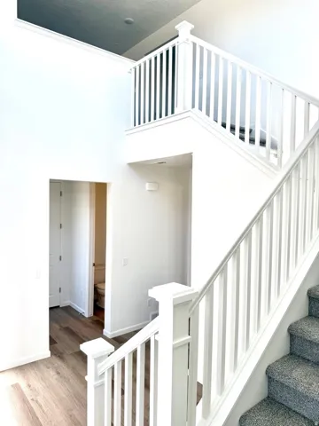 Two-story entry with white craftsman railing, wood-finish flooring, and carpeted staircase