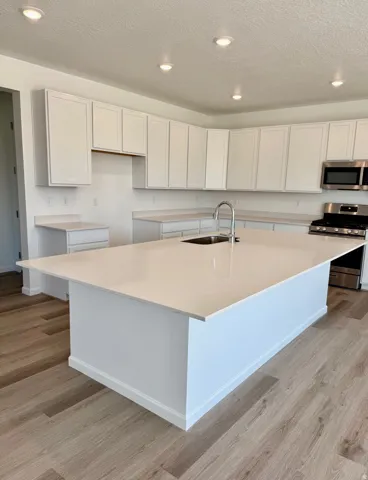 Expansive center island with an integrated sink, surrounded by white cabinetry and stone countertops, under recessed ceiling lighting, all set on LVT flooring