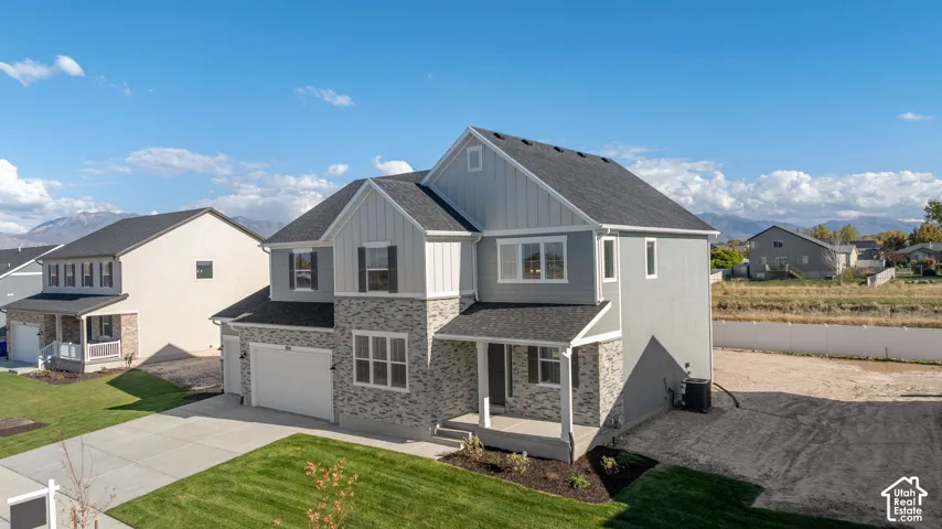 Two-story residence featuring a mixed-material facade of stone veneer and vertical siding, a covered front porch with a concrete stoop, a multi-gabled asphalt shingle roof, and an attached two-car garage