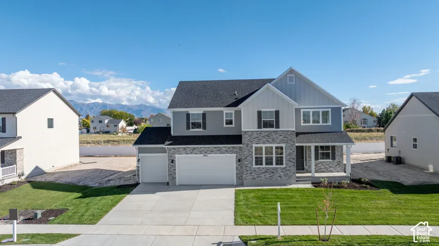 Two-story residence featuring a gray and white horizontal siding facade with stone veneer accents, a three-car garage, a covered front entryway, and mountain scenery