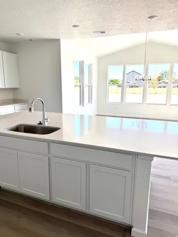 Kitchen island with undermount sink, white shaker-style cabinetry, and quartz countertop