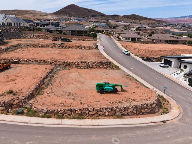 Graded residential lot featuring a paved road frontage, concrete sidewalks, and a rock retaining wall
