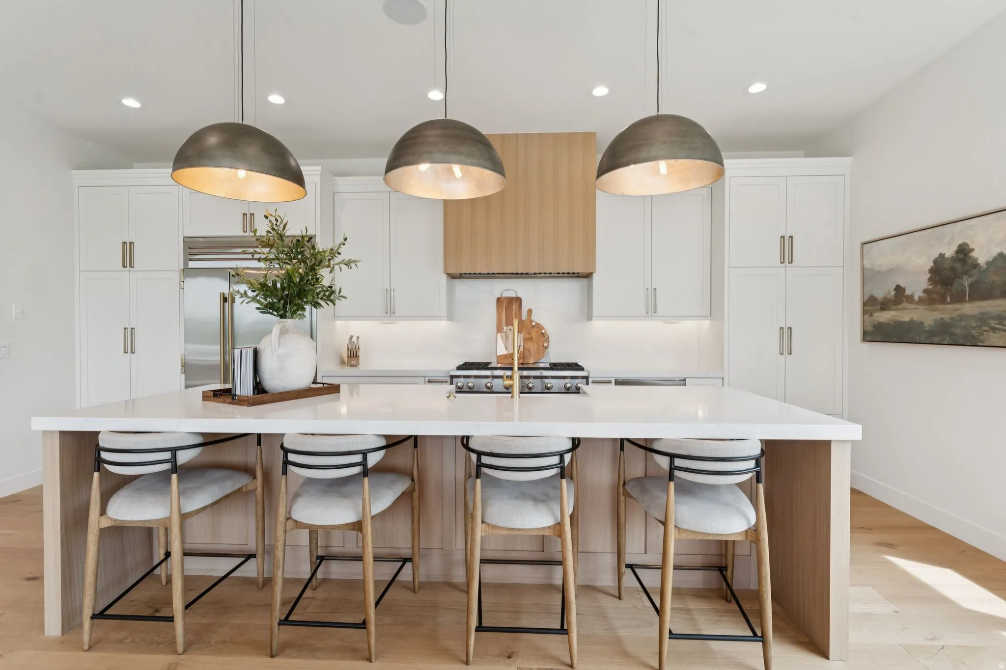 Kitchen featuring a large central island with seating, pendant lighting, white cabinetry, integrated stainless steel appliances, and wood-finish flooring