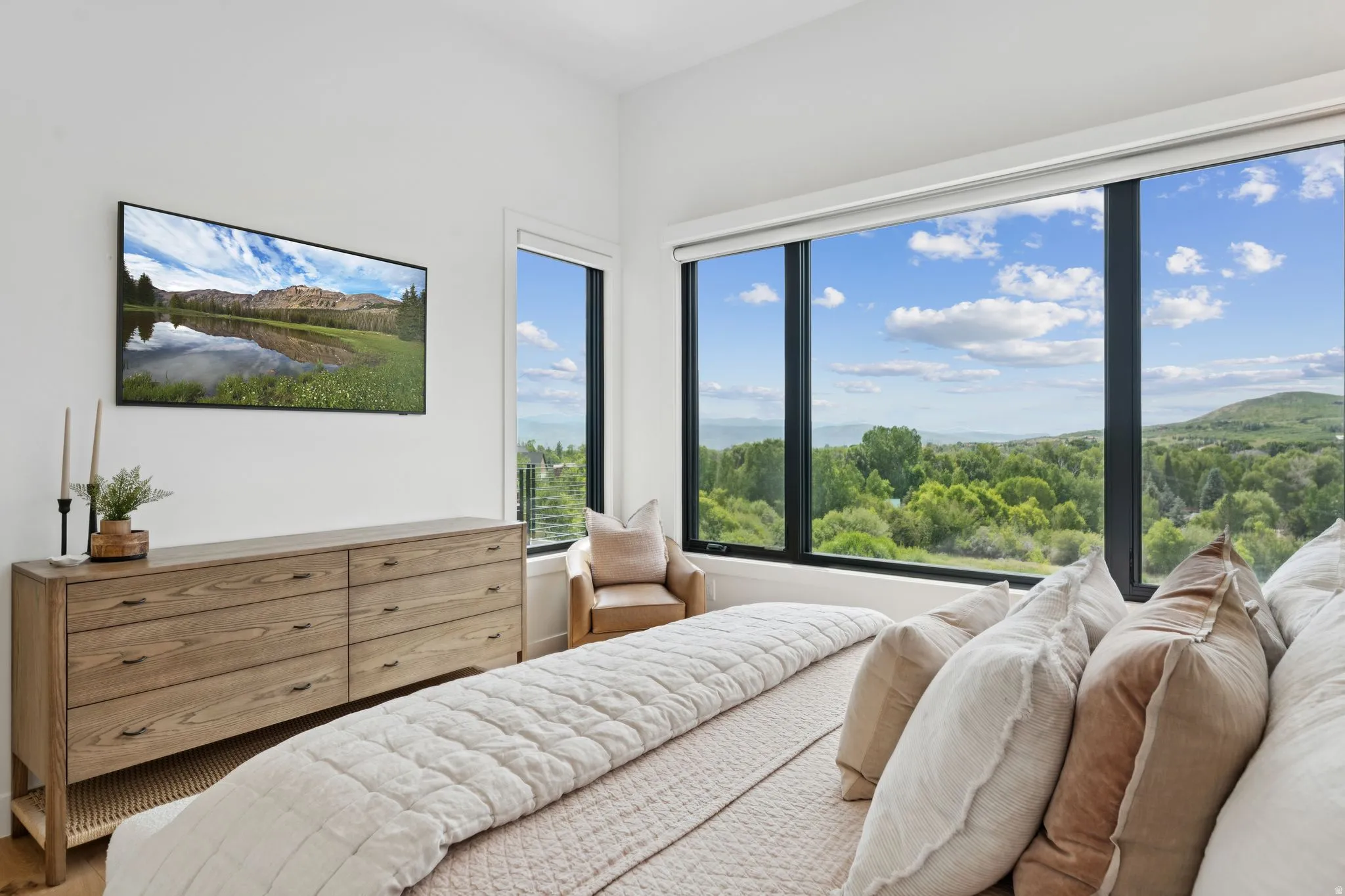 Expansive window wall with black framing, high ceilings, light wood-finish flooring, and a large wood-finish dresser with six drawers