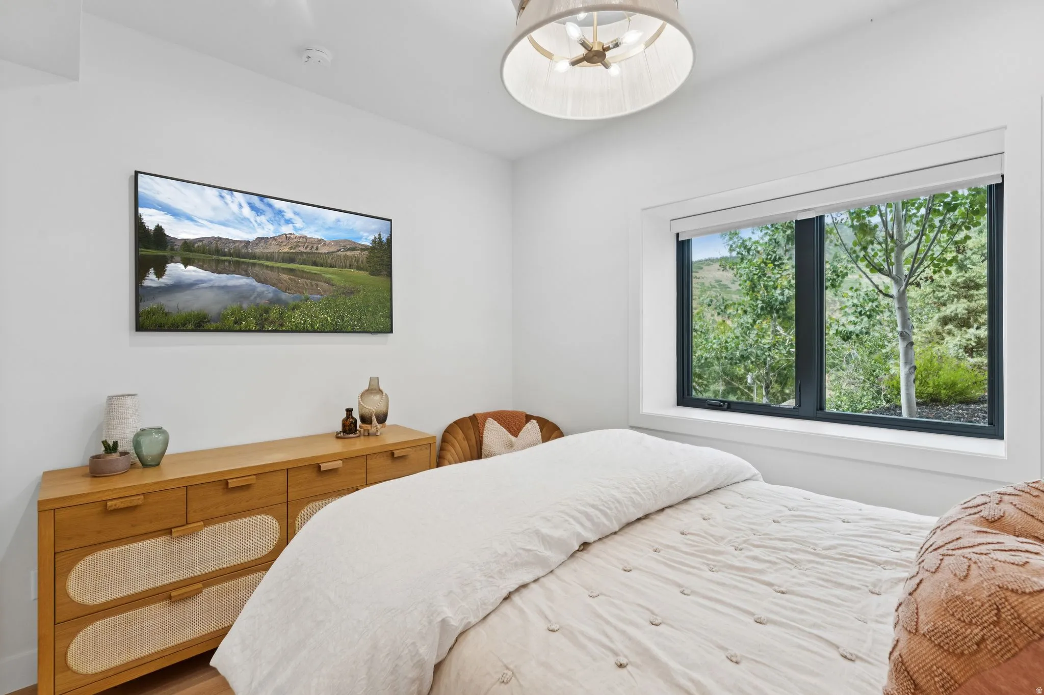 Bright interior featuring a built-in television, wood-finish flooring, a contemporary ceiling light fixture, and a large window with natural surroundings