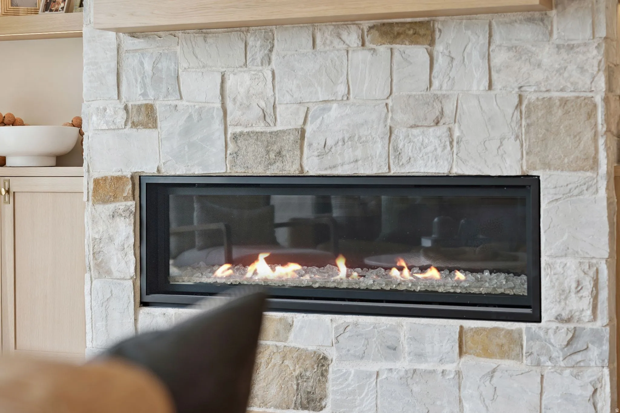 Stone fireplace featuring a linear gas insert with a black frame and decorative glass media