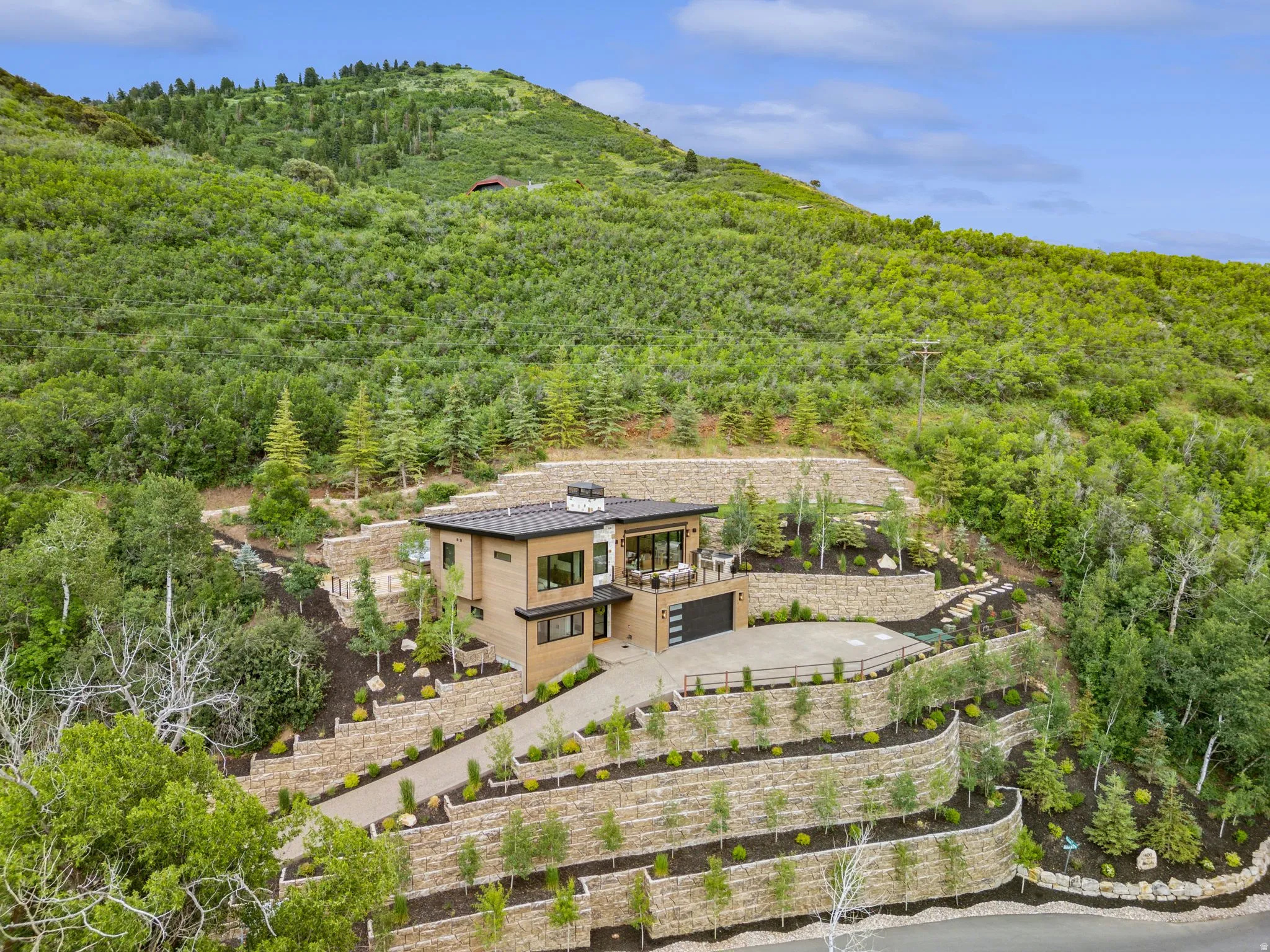 Modern residence featuring a flat roofline, wood-finish siding, and a multi-level terraced landscape with retaining walls