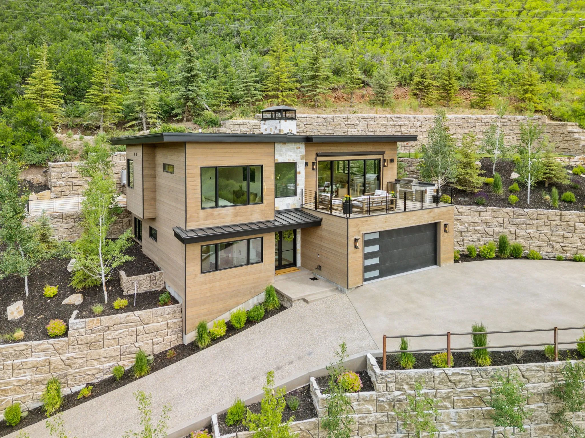 Contemporary multi-level exterior with wood-finish siding, stone accents, black-framed windows, and a flat roofline