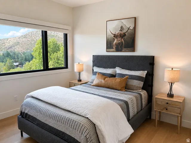 Bedroom featuring a horizontal window with black trim, light wood-finish flooring, and crisp white baseboards