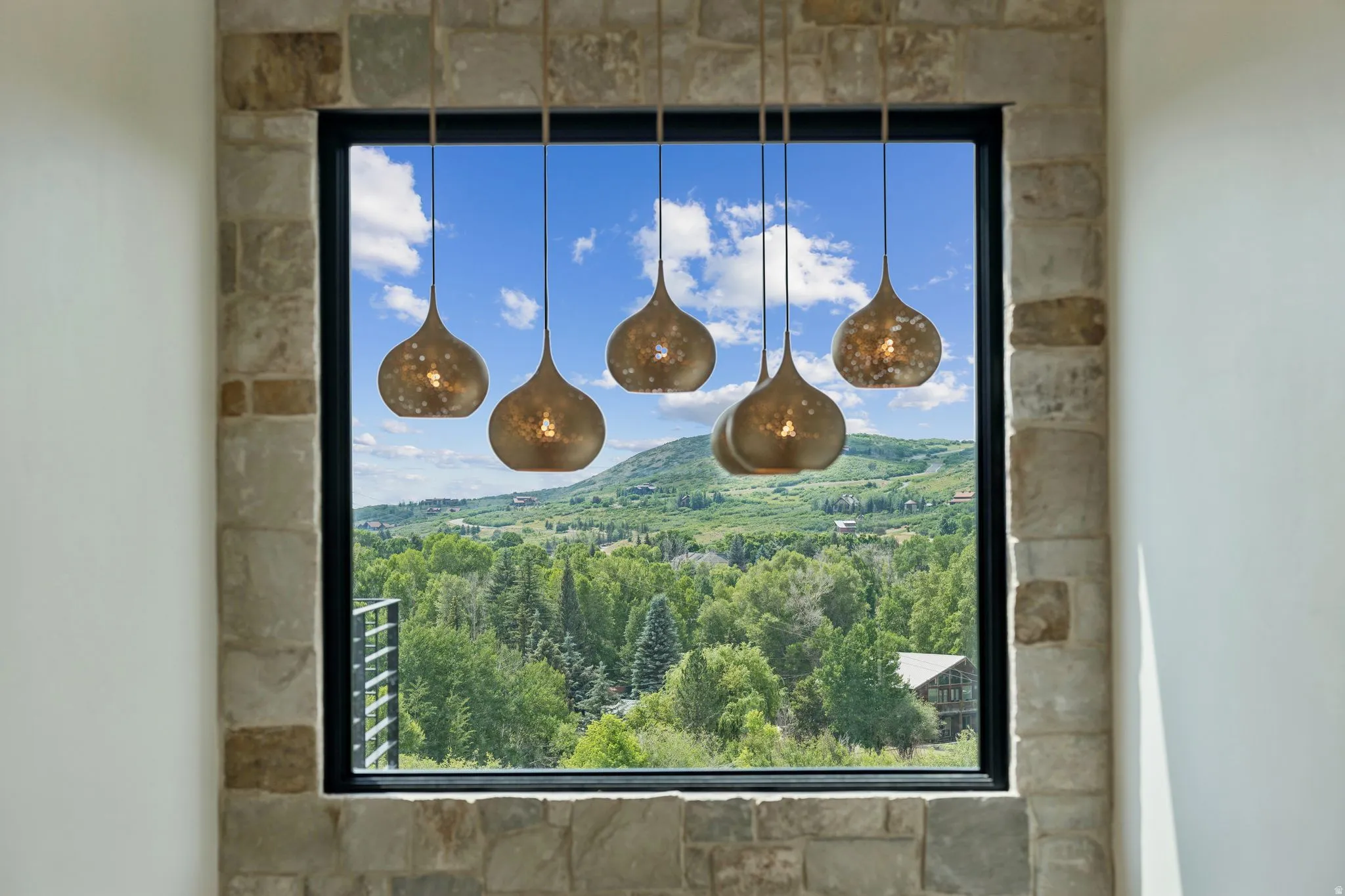 Stone-framed window featuring a five-light pendant fixture, showcasing a mountain landscape with abundant trees and a clear sky