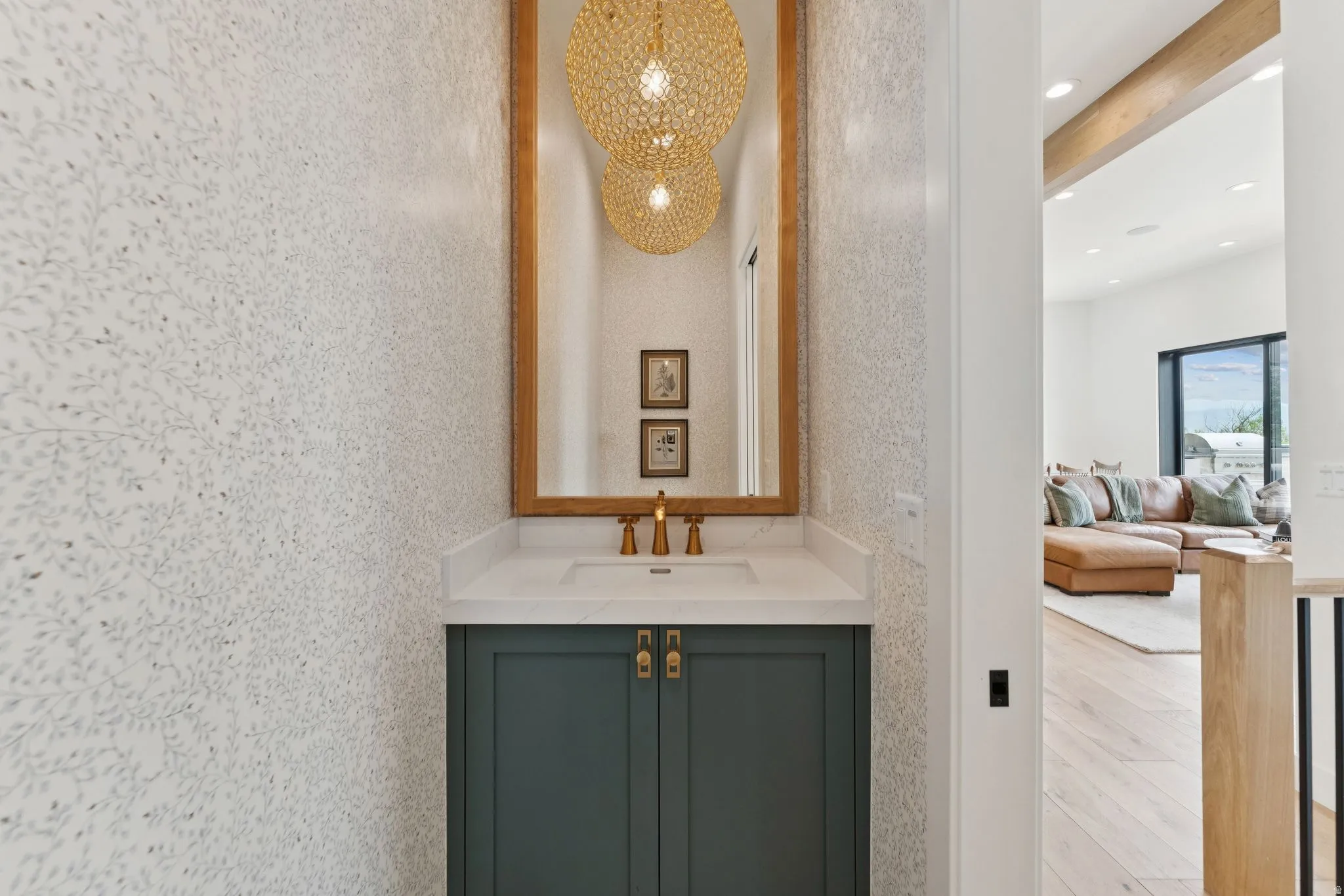 Powder room featuring botanical-patterned wallpaper, a wood-framed mirror, and a vanity with a white countertop and dark green cabinetry