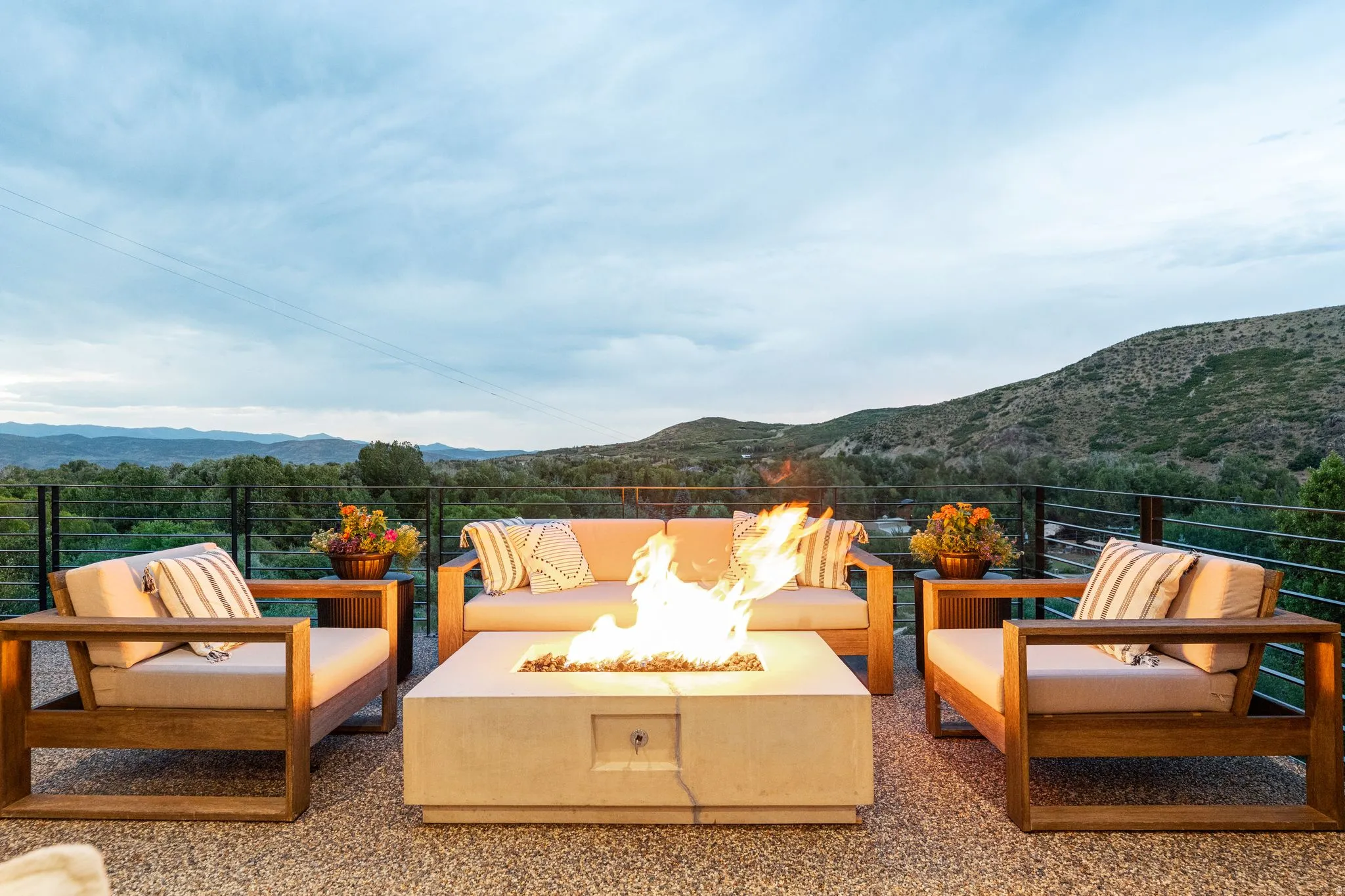 Expansive outdoor patio featuring a concrete fire pit, cable railing system, and a pebble-finish surface
