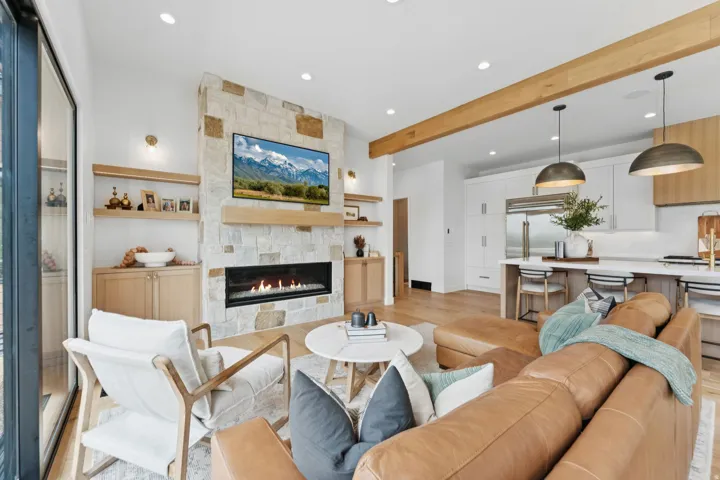 Open-concept living area featuring a stone-clad fireplace with a linear firebox, natural wood-finish mantel, and integrated built-in cabinetry with open shelving
