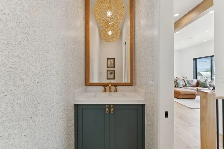 Powder room featuring botanical-patterned wallpaper, a wood-framed mirror, and a vanity with a white countertop and dark green cabinetry