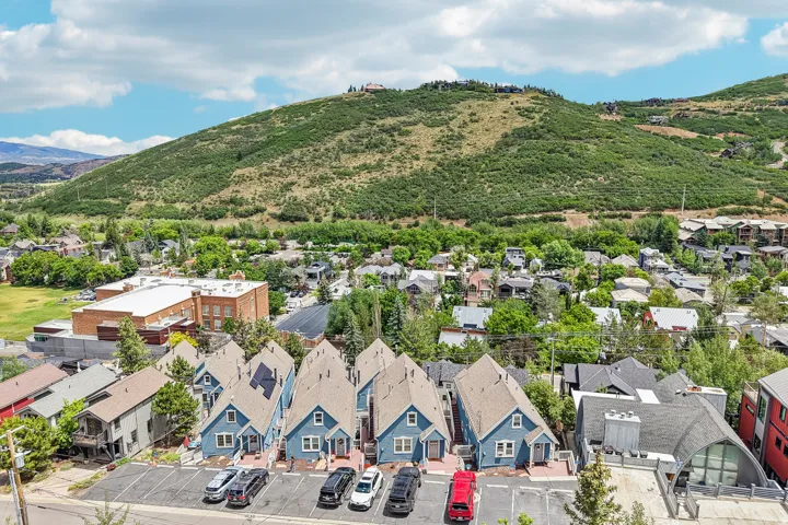 Row of blue residences with gabled roofs and individual parking spaces, set against a backdrop of verdant hills