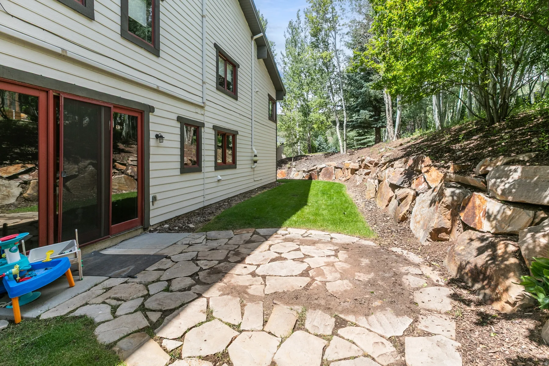 Outdoor flagstone patio with a rock retaining wall and green lawn