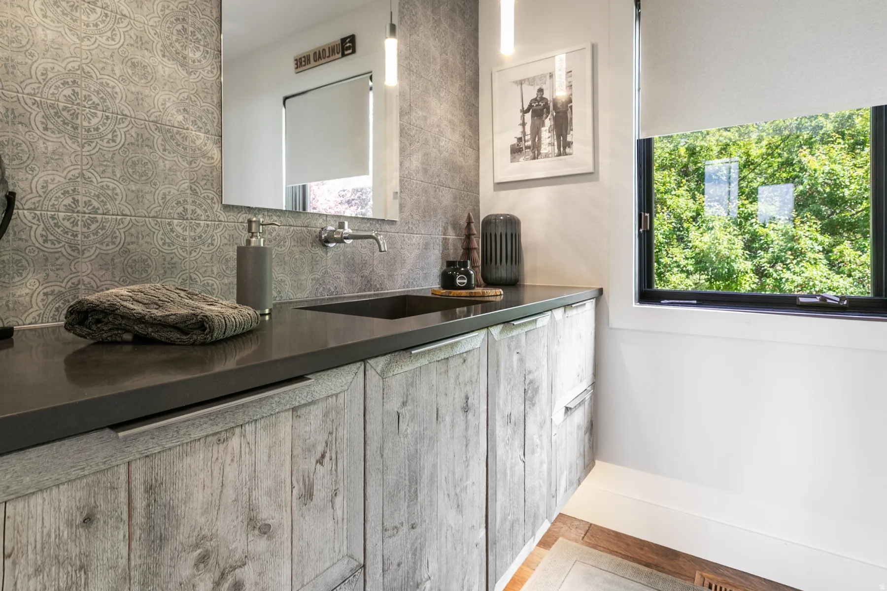 Modern bathroom featuring a wood-finish vanity with a dark countertop and integrated sink, wall-mounted faucet, patterned tile backsplash, and a large window