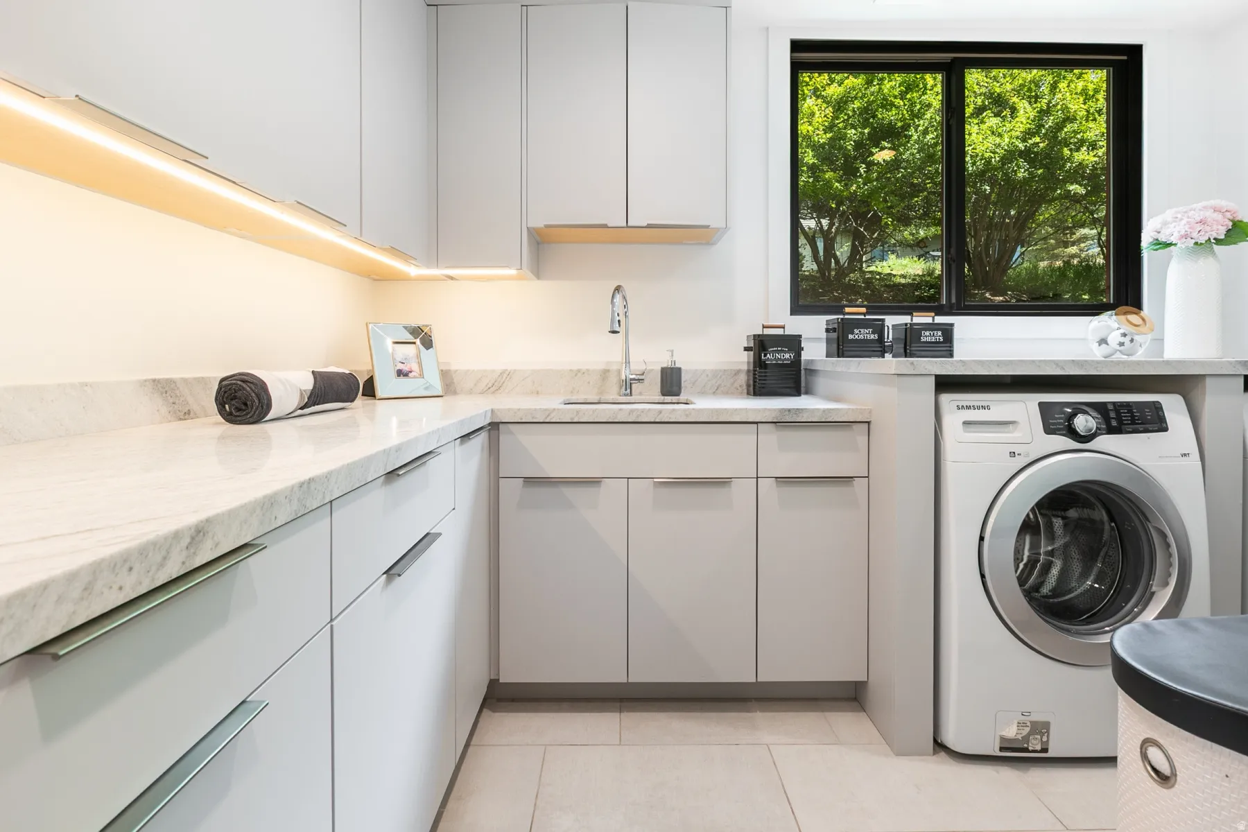 Contemporary laundry space featuring light-colored cabinetry, stone-finish countertops, and an undermount sink