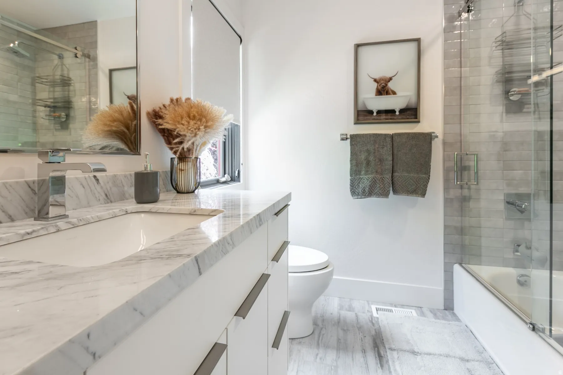 Bathroom featuring a white vanity with a stone countertop, an undermount sink with a chrome faucet, a large mirror, and a combination tub and shower with glass enclosure